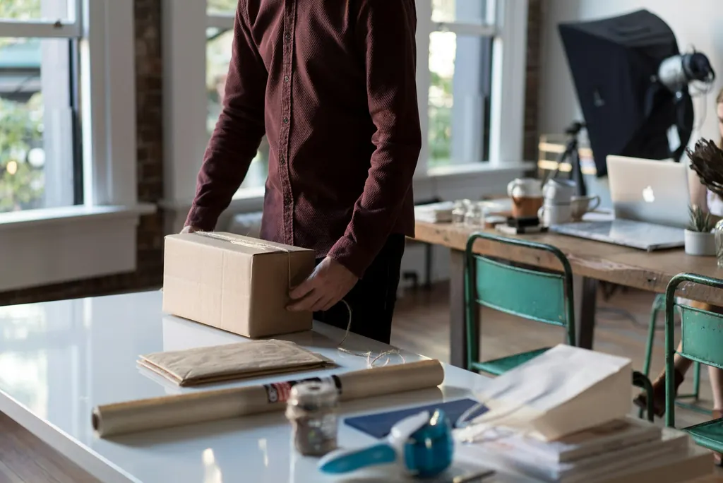 Small business owner packing a box at a bright studio desk